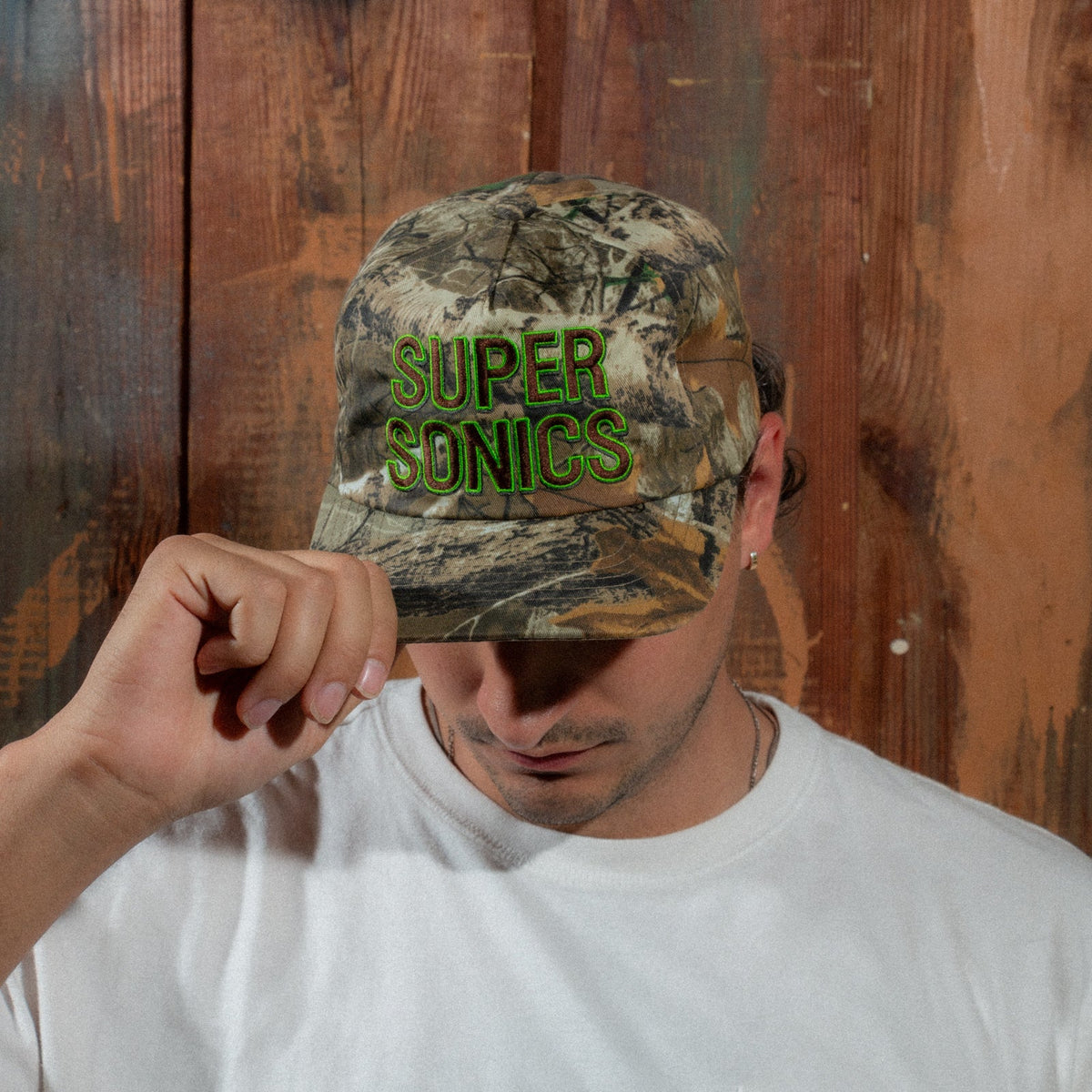 Model in a white T-shirt tipping the brim of the Peak Sonics Hat