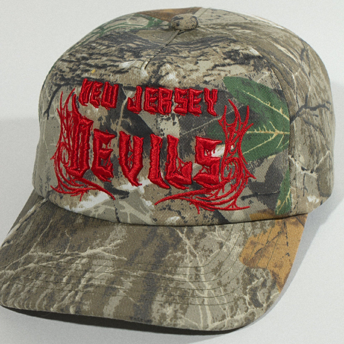 Close front shot from the left, with the red logo and camo brim filling the frame
