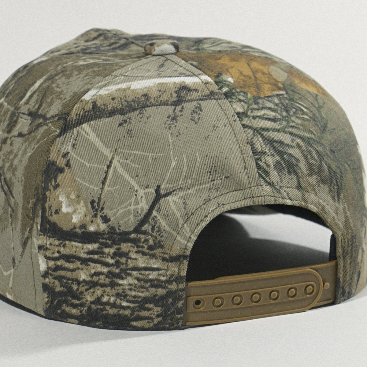Back of the hat showing the woodland camo panels and tan plastic snapback closure